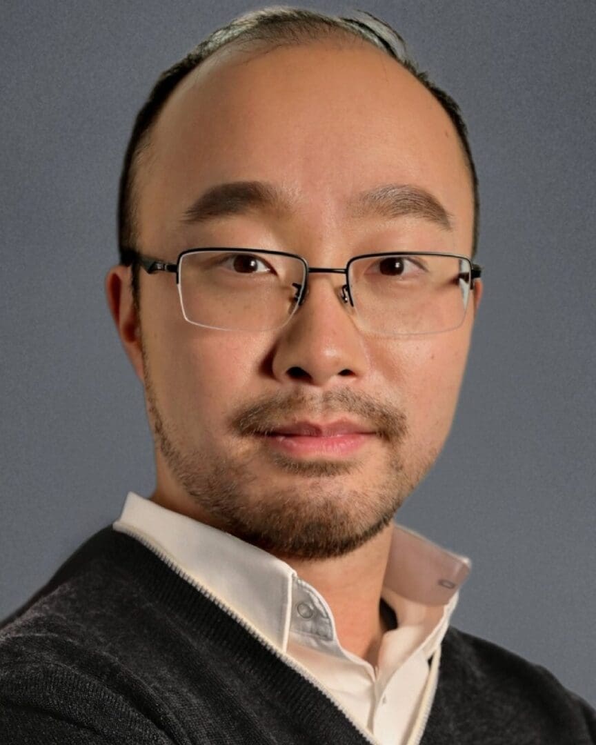 An asian man wearing glasses and a sweater.